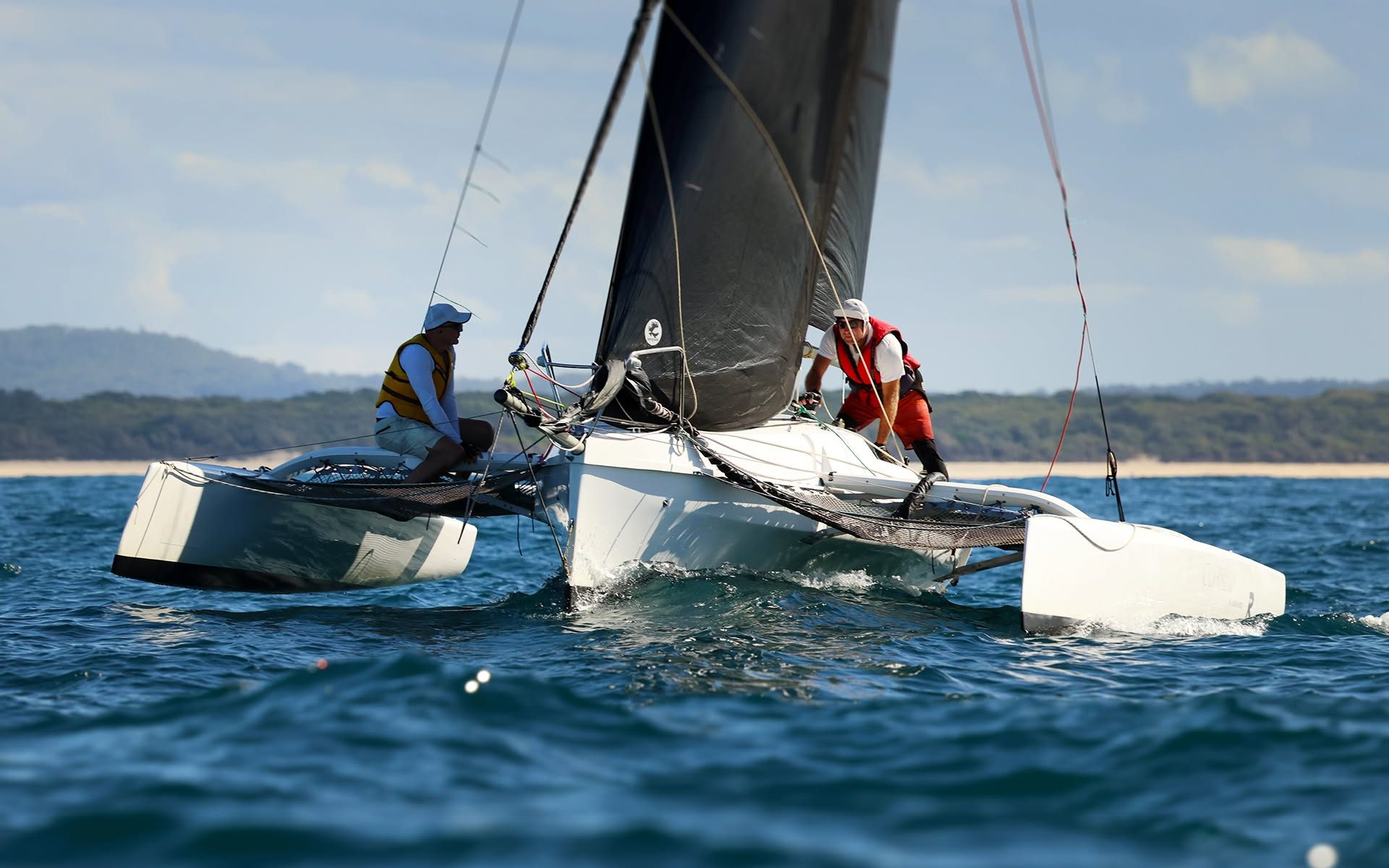 Two sailors racing a high-performance trimaran with a black mainsail on the waters of Port Stephens.